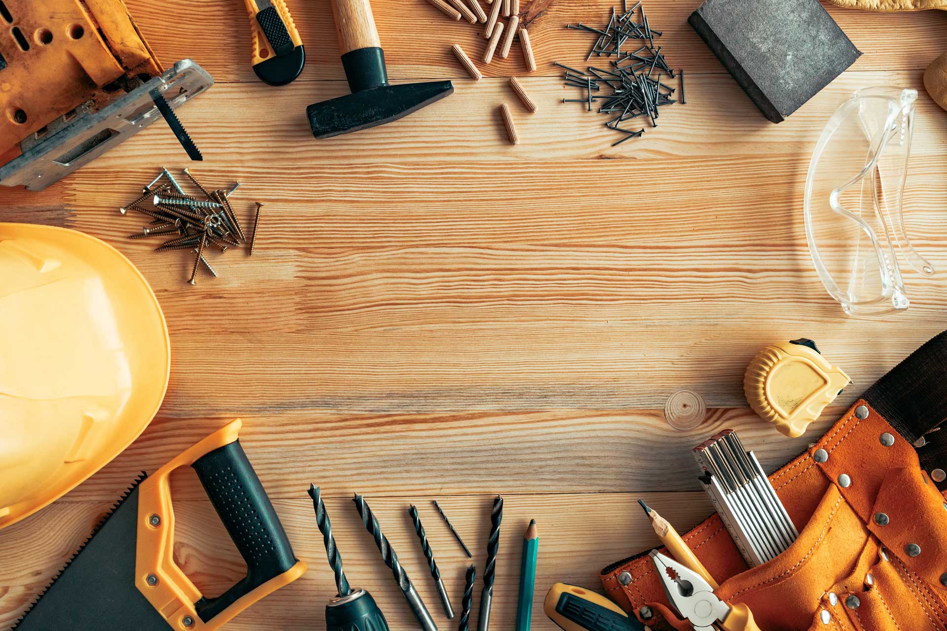 Repair supplies spread out on a bench including nails, screws, drill bits, a hardhat, a saw, safety goggles, a tape measure and a sanding block